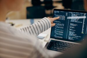 Close up of female software engineer writing code on laptop with screens setup in coworking