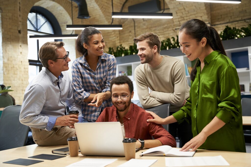 Group of young happy business people looking at laptop screen, communocating and discussing work